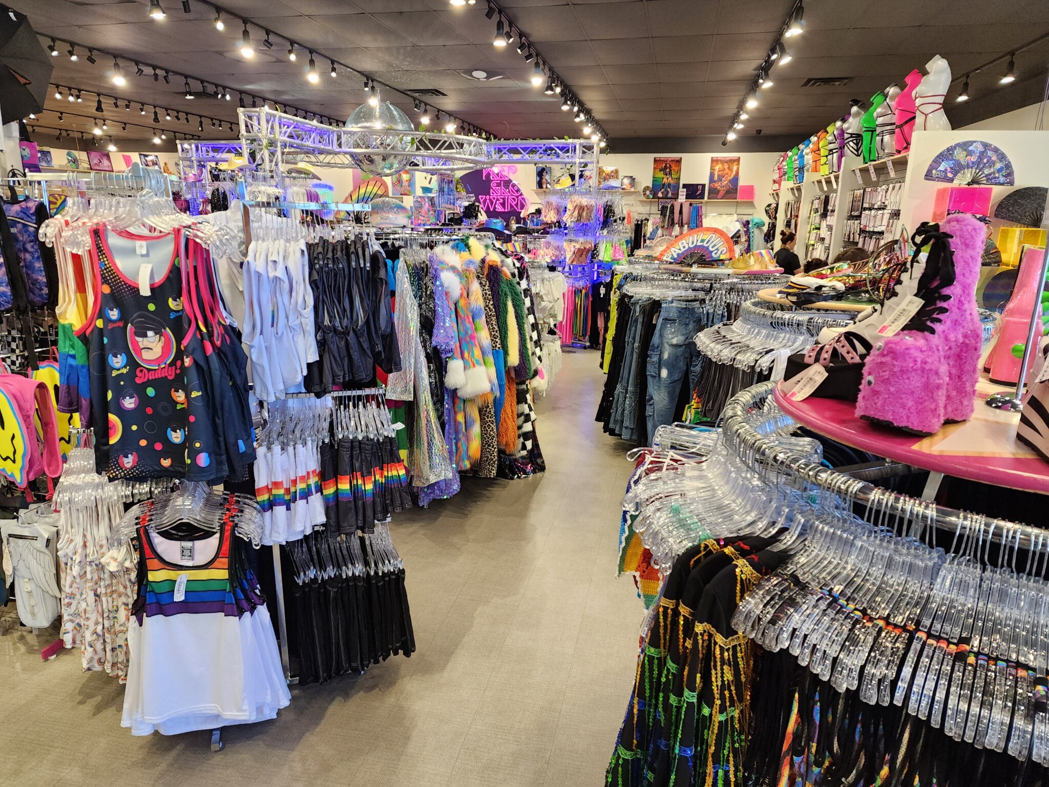 A vibrant display inside iconoCLAD, showcasing a colorful array of new items for the 2024 Utah Pride festival. The shop is adorned with rainbow pashminas, sparkling bio-glitter sunscreen, face and body gems, and a variety of flags, patches, and pins. The eclectic mix of chic outfits and accessories highlights the store’s unique and inclusive fashion vibe, ready to celebrate Pride in style.